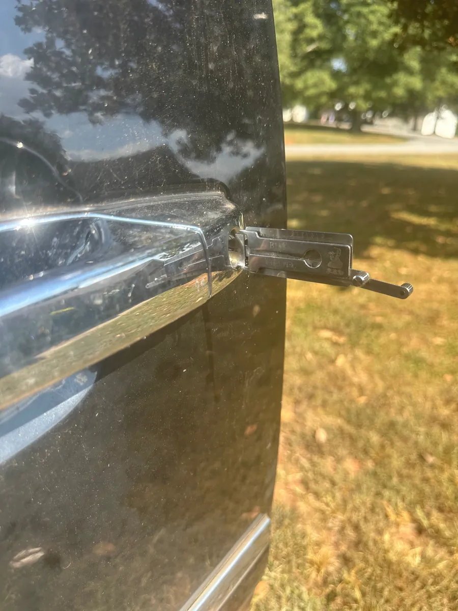 A slim tool at the door lock of a black car parked on the grass