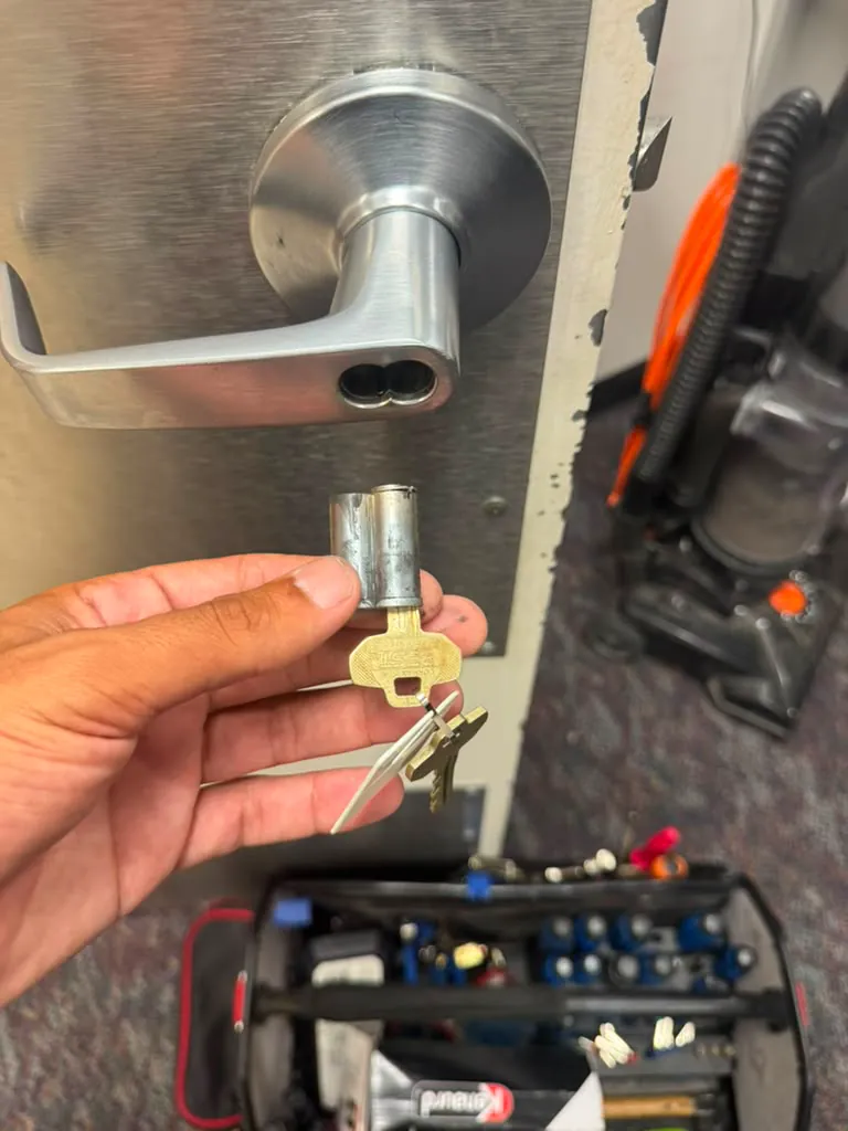 Hand holding a lock cylinder and keys beside the lever handle of an office door