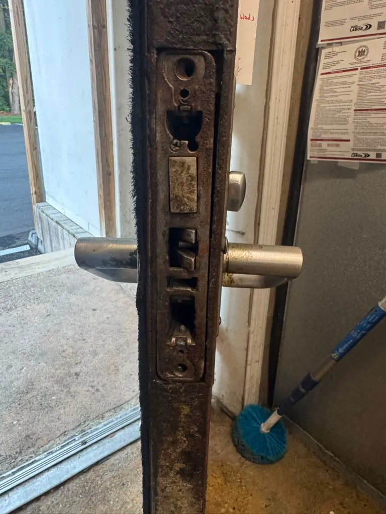 Edge of a commercial door with the lock body exposed and the lever handles in place